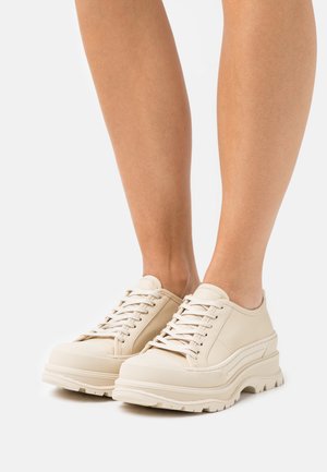 Beige snøresko laget av glatt lær, med en tykk, teksturert såle og rund tådesign. Minimalistisk stil med subtile sømdetaljer.