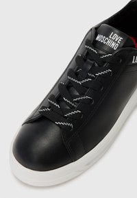 Black leather sneaker with white-trimmed black laces, white sole, and "LOVE MOSCHINO" logo on the tongue and side.