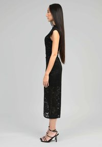 Robe en dentelle noire avec une silhouette ajustée, des manches courtes et un ourlet mi-long. Présente une section en dentelle transparente en bas et des sandales à talons fins.