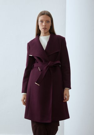 Manteau en mélange de laine bordeaux avec larges revers, taille ceinturée et accents en métal argenté. Manches longues et longueur en dessous du genou. Texture lisse.