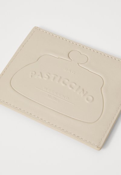 Bežs ādas kredītkartes turētājs ar iegrieztu "PASTICCINO" logotipu, apaļais aizdare augšpusē un redzami vīlējumi gar malām.