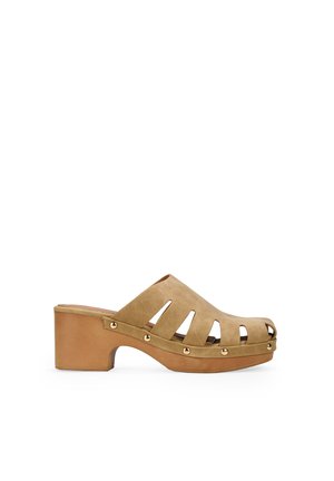 Mules de plataforma de ante marrón con diseño recortado y puntera redonda, con tachuelas metálicas a lo largo de la base. Textura suave con un tacón grueso.