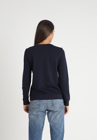 Námořnicky modrá mikina s dlouhými rukávy, kulatým výstřihem, úzkým střihem a žebrovanými manžetami. Zadní strana je bez ozdob, s jednoduchým designem.