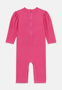 Ružičasti kombinezon s dugim rukavima, visokim ovratnikom i patentnim zatvaračem straga. Glatka tekstura, dizajniran s uskim nogavicama i otvorom na dnu.