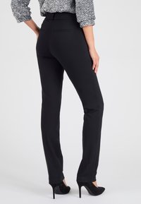 Zwarte op maat gemaakte broeken met een slim fit en een gladde textuur. Voorzien van een middelhoge taille en twee achterzakken, gecombineerd met zwarte hoge hakken.