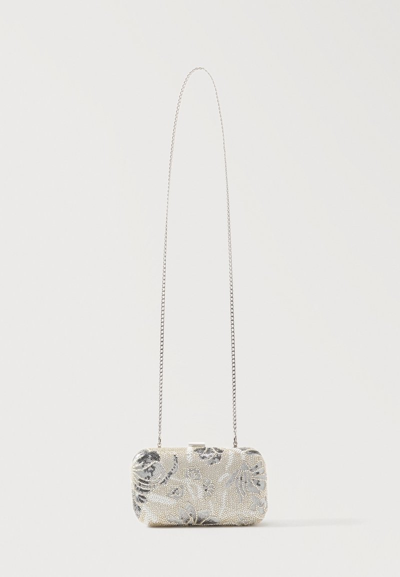 Petit sac clutch rectangulaire avec perles florales argentées et une fine bandoulière chaîne sur un fond clair uni.