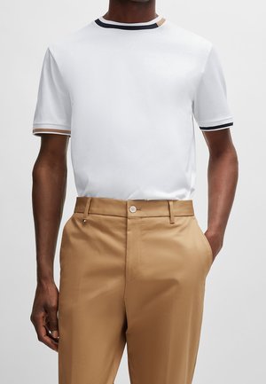 Biała koszulka z krótkim rękawem z kontrastującymi granatowymi i beżowymi prążkowanymi wykończeniami na kołnierzu i rękawach, zestawiona z beżowymi, dopasowanymi spodniami.