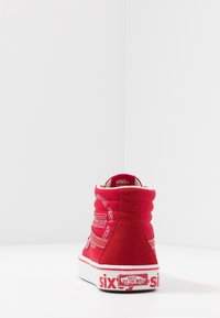 Baskets montantes rouges en suède avec des accents blancs. Présente le logo Vans et des détails de motifs sur le talon et le côté. Semelle en caoutchouc.