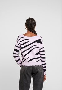 Sweter dzianinowy w kolorze liliowym z czarnymi paskami w zebry. Posiada szeroki dekolt i postrzępiony brzeg, w zestawieniu z jeansami o wysokim stanie.