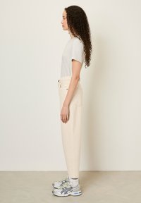 Pantalons beiges taille haute en coton, avec deux poches avant et deux poches arrière, associés à un t-shirt gris clair et des baskets.