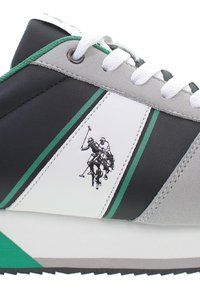 Sportowe sneakersy z mieszanką czarnych, szarych i białych materiałów z zielonymi akcentami. Wyróżniająca się wytłoczona grafika gracza polo po stronie.