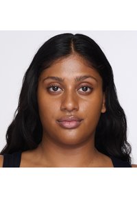Porträtt av en person med långt, mörkt hår, medelbrun hud och naturlig makeup. Drag inkluderar framträdande ögon, fylliga läppar och en jämn hy.