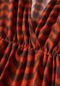 Rot-schwarzer Stoff mit Zickzackmuster, elastischem Gummibund und überlappendem V-Ausschnitt.