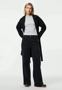 Pantaloni di jeans neri a gamba larga abbinati a un maglione a coste grigio chiaro e a un lungo cappotto nero. Caratteristiche includono una vita alta e tasche anteriori.