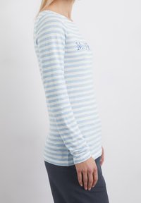 Pitkähihaisen vaaleansinisen ja valkoisen raidoituksen omaavan paidan, joka on valmistettu pehmeästä kankaasta. Paidassa on veneen muotoinen kaula-aukko ja painettu kuvio rinnassa.