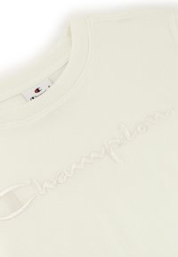 Light-colored cotton T-shirt featuring an embroidered "Champion" logo in a subtle, contrasting thread. Classic crew neckline, soft texture.