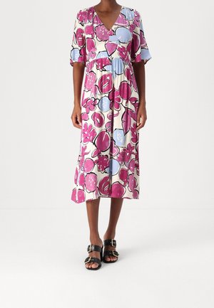 Woman wearing a V-neck, short-sleeve midi dress with pink and blue abstract floral print, paired with black buckle sandals.
