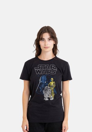 Young woman wearing a black Star Wars t-shirt featuring Darth Vader, C-3PO, and R2-D2 on a plain white background.