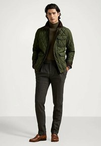 Κουκουλωτή ελιάς χρώματος σακάκι με καφέ γιακά, σε συνδυασμό με σκούρο λαιμόκοψη, γκρι παντελόνι και καφέ παπούτσια. Διαθέτει τσέπες και υφή υφάσματος.