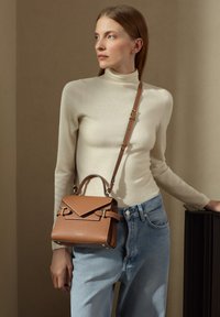 Bolso de mano de cuero marrón con un diseño estructurado, tapa plegable, detalles en oro y un asa corta más una correa de hombro ajustable.