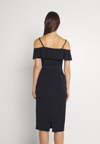 Vestido azul-marinho com detalhe de babados off-the-shoulder, corpete de renda e saia lápis com fenda nas costas e fecho de zíper.
