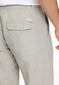 Ljust grå linnebyxor med en bakficka som har en klaff, subtil textur och en etikett som är sydd nära fickan. Avslappnad passform och lättviktig tyg.