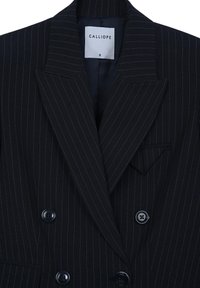 Blazer a righe navy realizzato in tessuto testurizzato, con rever a punta, bottoni doppi e una piccola tasca sul petto. Etichetta del marchio visibile.