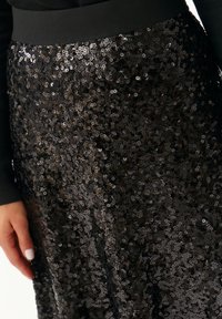 Gonna nera di paillettes con una texture liscia e una superficie lucida, dotata di una ampia vita nera e di paillettes circolari densamente raccolte.