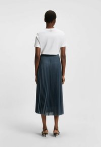 Witte kortekoe shirts met "BOSS" branding op de rug, gecombineerd met een donker geplooide midi rok en zwarte haksandalen.