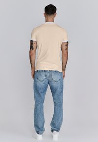 Beige T-shirt met witte mouwaccenten, gecombineerd met lichtblauwe denim jeans en witte sneakers, met een casual pasvorm en zachte textuur.