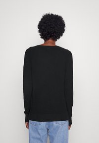 Maglione nero texturizzato con maniche lunghe e scollatura ampia, indossato sopra jeans azzurri chiari. Mostra la vista posteriore con un design leggermente accorciato.