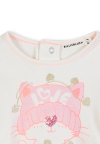 Biała bawełniana koszula z różowym graficznym motywem kota w błyszczącej czapce i serduszkach, akcentowana małymi złotymi detalami i zapięciem na napę.