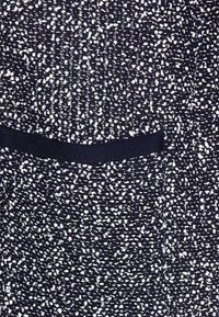 Granatowa tkanina o fakturze z nakrapianym wzorem z białymi kropkami; zawiera detal w postaci kieszeni z ciemnej tkaniny.