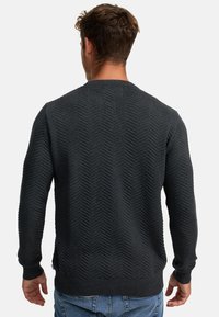 Mørkegrå sweater med et struktureret hørhåndmønster, ribbet halsudskæring ogmanchetter samt sidesplitter, parret med lyseblå jeans.