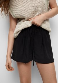 Svarta shorts med dragsko och avslappnad passform, gjorda av mjukt tyg; bärs med en löst stickad beige topp med texturerad väv.