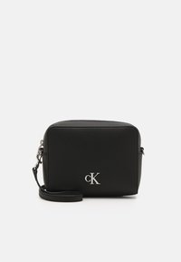 Borsa a tracolla rettangolare nera in pelle testurizzata, caratterizzata da un logo "cK" in argento e una tracolla regolabile con gancio in metallo.