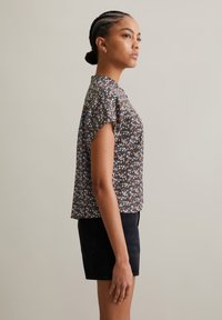 Zwarte bloes met korte mouwen, met veelkleurige bloemen op een donkere achtergrond. Gecombineerd met zwarte denim shorts.