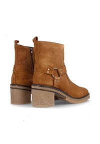 Botines de ante en tono beige con cremallera lateral, una banda ancha y detalle de anillo, y un tacón grueso texturizado en color beige. Acabado suave y mate.