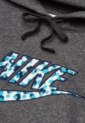 Šedá mikina s kapucí, která má výrazné modro-bílé tie-dye logo Nike. Černé šňůrky doplňují texturovanou látku.
