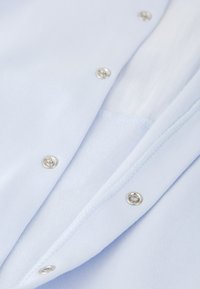 Camisa de tela azul claro con botones a presión plateados, con una textura suave y costuras bien hechas a lo largo de los bordes.