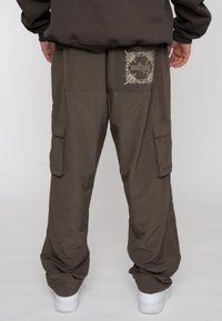 Olijfgroene cargobroek van lichtgewicht stof, voorzien van een grafische patch, twee zijzakken en taps tolopende benen met elastische boorden.