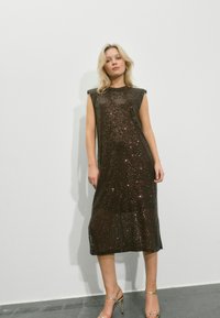 Gnistrande brun midi-klänning med kappärmar och en rak siluett. Texturerat tyg med paljetter. Matchad med silvriga sandaletter med klack.