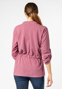 Rosa Langarm-Oberteil mit cinchtem Taillenschnitt und hochgerollten Ärmeln. Weicher Stoff und lockere Passform, mit einem schlichten Design.