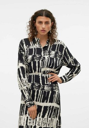 Robe à motifs noir et blanc avec un col, des manches longues et une coupe décontractée. Le tissu a une texture lisse et un design abstrait remarquable.