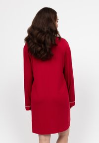 Abito rosso a maniche lunghe con vestibilità comoda, caratterizzato da dettagli bianchi ai polsini. Tessuto liscio, design lungo fino al ginocchio e silhouette semplice.