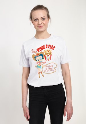 Hvid t-shirt med en tegneseriefigur med blåt hår, iført en cowboyhat og røde detaljer, med teksten "Betty's WINGS O'FIRE" i rødt.