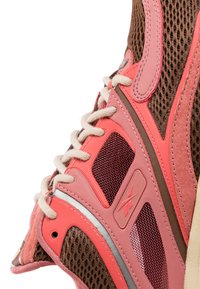 Brown and pink athletic shoe with mesh and synthetic materials, featuring prominent lacing, textured accents, and a distinct logo.