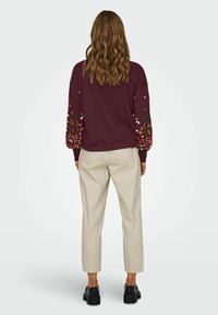 Felpa bordeaux con ricami floreali sulle maniche a sbuffo, abbinata a pantaloni beige a sigaretta e scarpe platform nere.