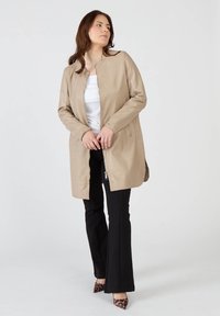 Beige läderjacka med rund hals, framdragkedja, sidofickor och en något förlängd skärning, kombinerad med svarta utsvängda byxor och klackar i djurtryck.