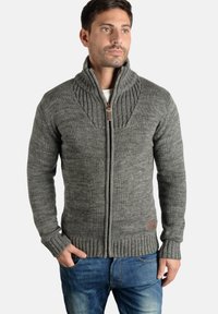 Suéter gris de punto con cuello alto, con puños y dobladillo de canalé. Parte frontal con cremallera y un pequeño acento de cuero en la parte inferior izquierda.